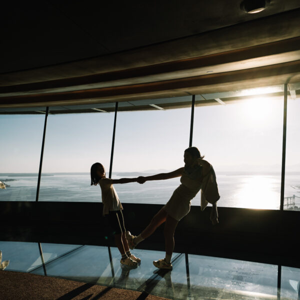 Two people holding hands and leaning back with their body weight on the Loupe rotating glass floor